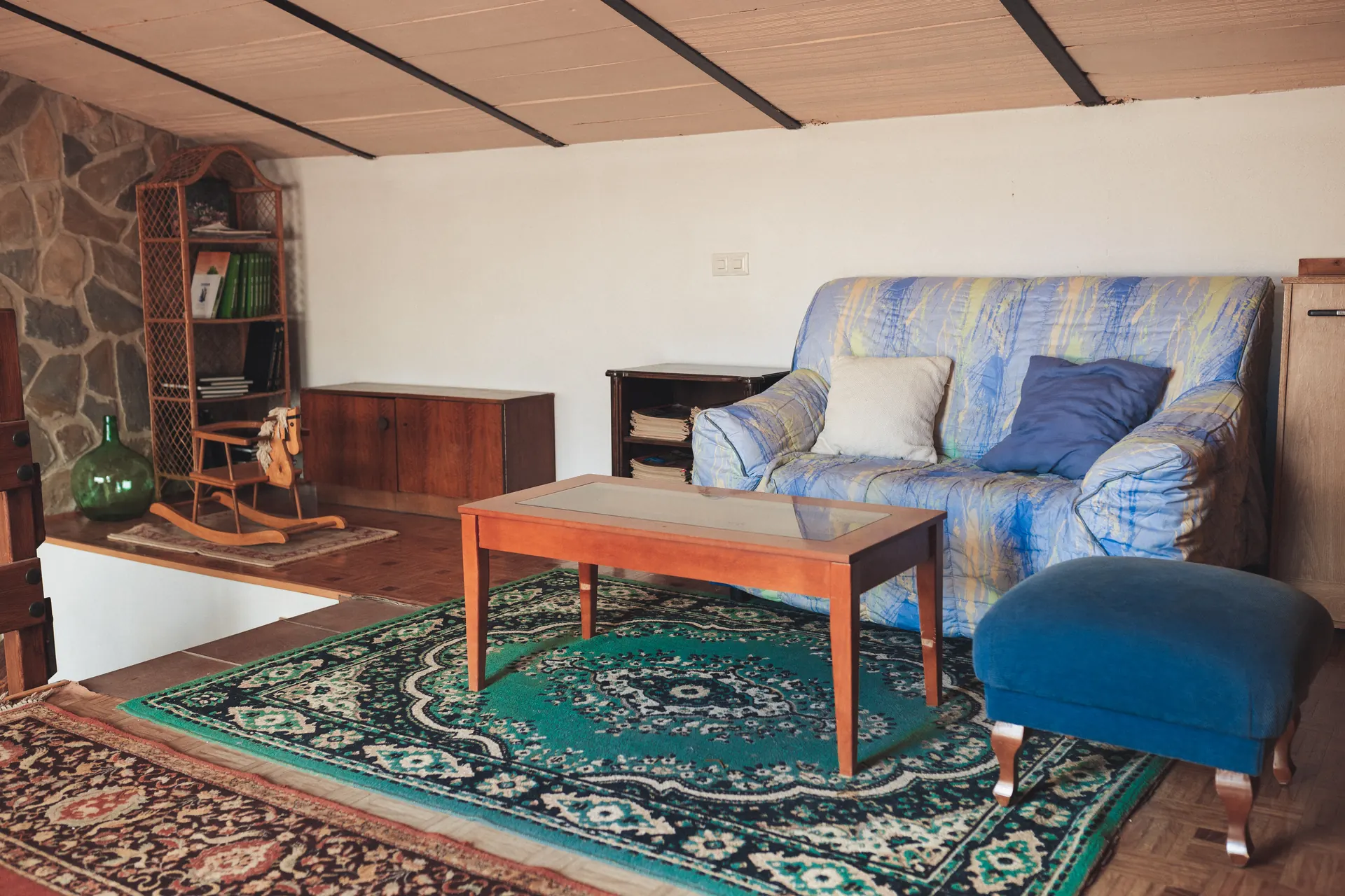 Sala con techo de madera, sofá azul y alfombra estampada junto a la azotea
