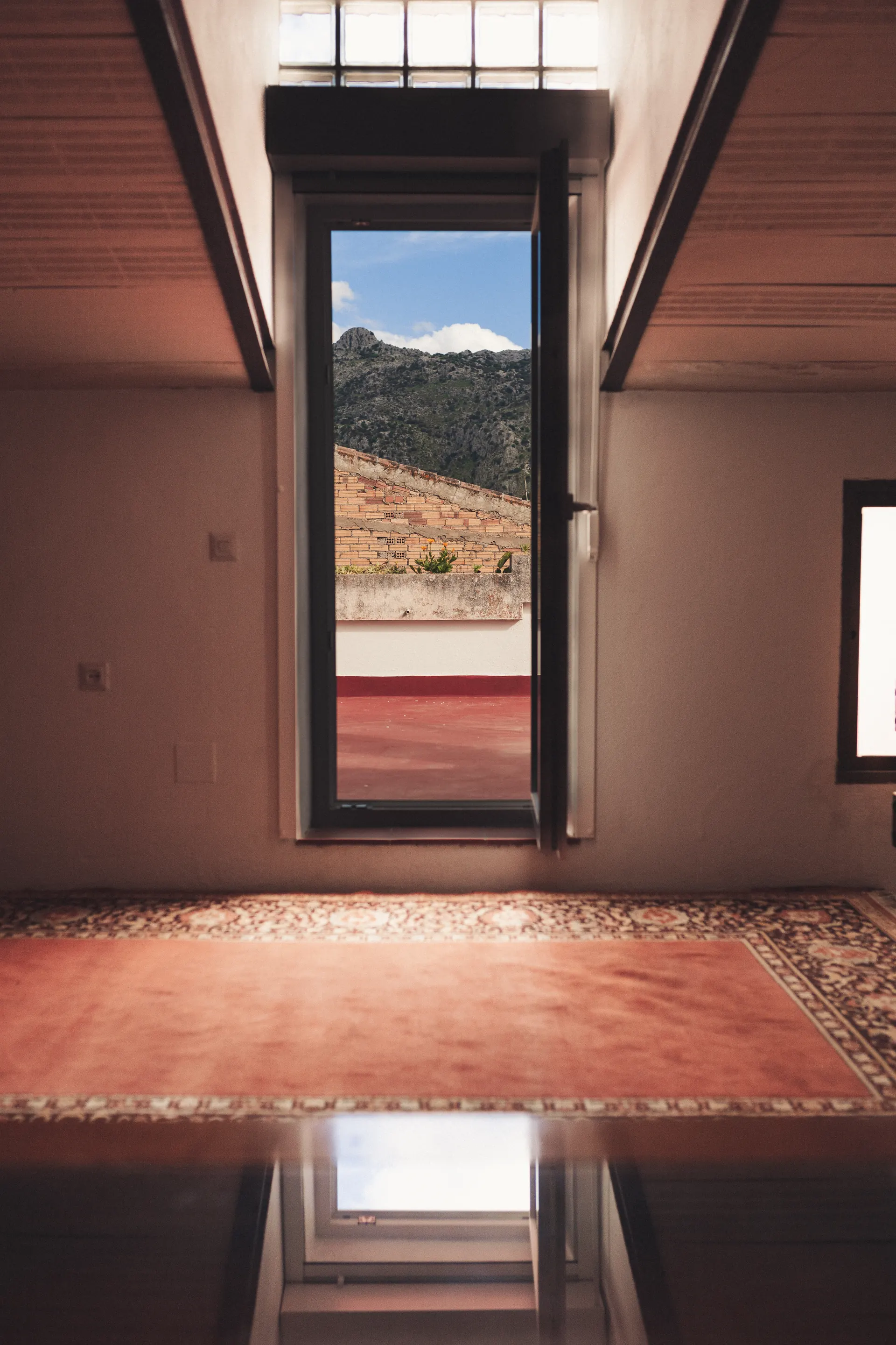 Ventanal de una habitación abierto a la azotea y la sierra al fondo
